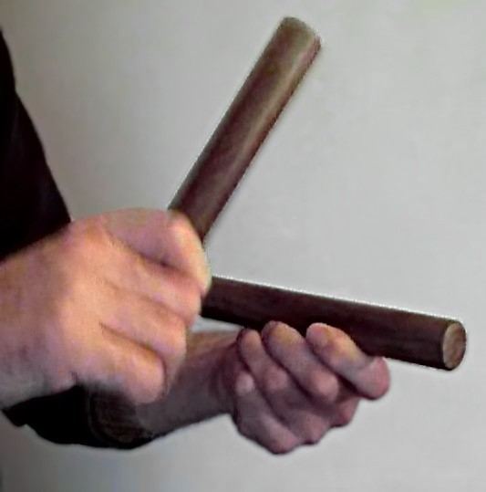 Zwei Hände halten zwei runde Holzstäbe, die aneinandergeschlagen werden